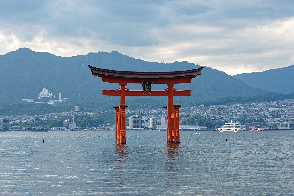 The great torii gate of Itsukushima Shrine standing in the sea at Miyajima, with mountains and a town behind it